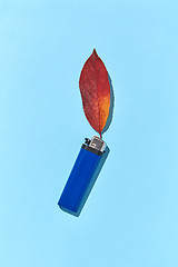 Image showing Creative composition blue lighter with fire from fall red leaf and hard shadows.