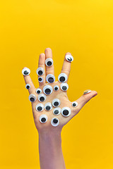 Image showing Woman\'s hand with plastic eyes on an yellow background.