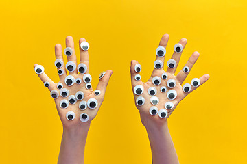 Image showing Two girl\'s hands with plastic eyes on an yellow background.