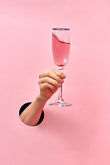 Image showing Rose wine glass in a female\'s hand from the hole in the wall.