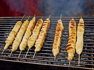 Image showing Meat dish wrapped in dough around wooden sticks is grilled