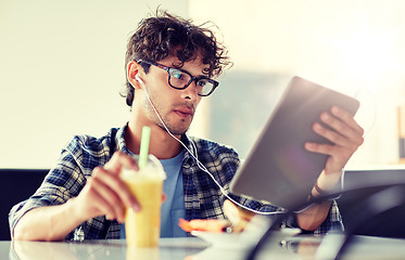 Image showing man with tablet pc and earphones sitting at cafe