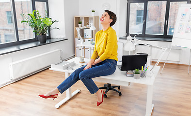 Image showing happy businesswoman sitting on desk at office