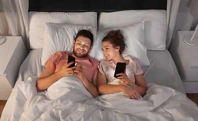 Image showing happy couple using smartphones in bed at night