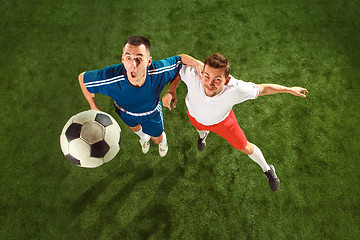 Image showing Football players tackling for the ball over green grass background