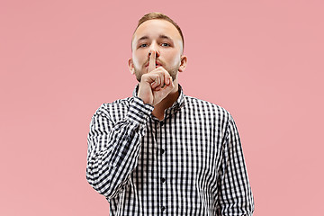 Image showing The young man whispering a secret behind her hand over pink background