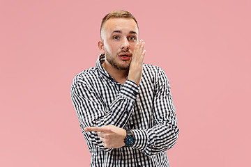 Image showing The young man whispering a secret behind her hand over pink background