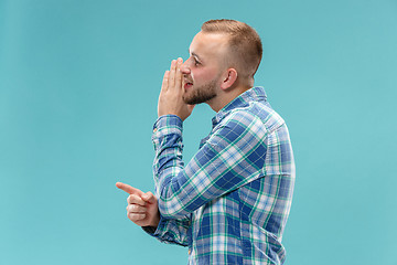 Image showing The young man whispering a secret behind her hand over blue background