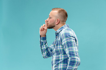 Image showing The young man whispering a secret behind her hand over blue background