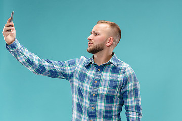 Image showing Portrait of attractive young man taking a selfie with his smartphone. Isolated on blue background.