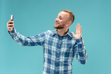 Image showing Portrait of attractive young man taking a selfie with his smartphone. Isolated on blue background.