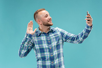 Image showing Portrait of attractive young man taking a selfie with his smartphone. Isolated on blue background.