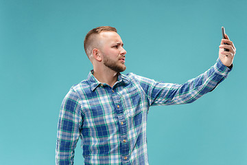 Image showing Portrait of attractive young man taking a selfie with his smartphone. Isolated on blue background.