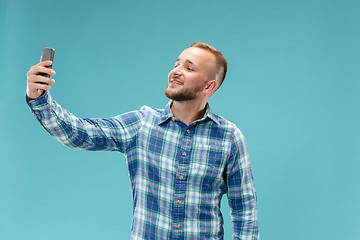 Image showing Portrait of attractive young man taking a selfie with his smartphone. Isolated on blue background.