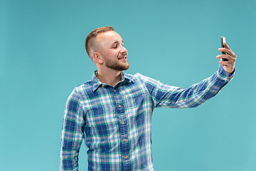 Image showing Portrait of attractive young man taking a selfie with his smartphone. Isolated on blue background.