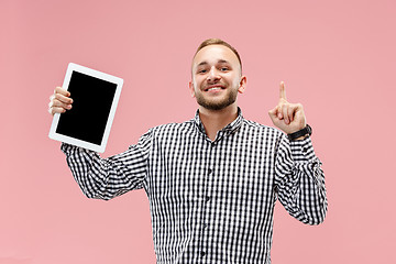 Image showing Studio picture of positive man isolated on pink background standing in casual clothes holding tablet and showing it blank screen with happy smile