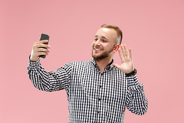 Image showing Portrait of attractive young man taking a selfie with his smartphone. Isolated on pink background.