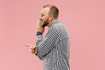 Image showing The young man whispering a secret behind her hand over pink background