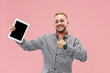 Image showing Studio picture of positive man isolated on pink background standing in casual clothes holding tablet and showing it blank screen with happy smile