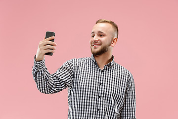 Image showing Portrait of attractive young man taking a selfie with his smartphone. Isolated on pink background.