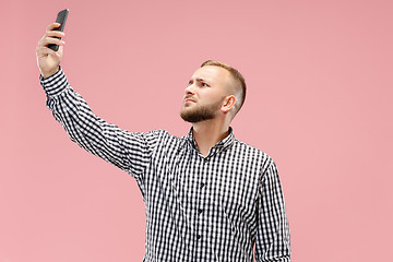 Image showing Portrait of attractive young man taking a selfie with his smartphone. Isolated on pink background.