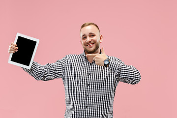 Image showing Studio picture of positive man isolated on pink background standing in casual clothes holding tablet and showing it blank screen with happy smile