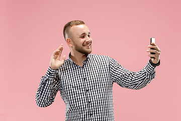 Image showing Portrait of attractive young man taking a selfie with his smartphone. Isolated on pink background.