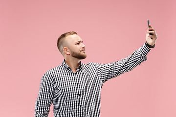 Image showing Portrait of attractive young man taking a selfie with his smartphone. Isolated on pink background.