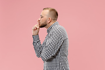 Image showing The young man whispering a secret behind her hand over pink background