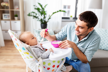 Image showing father feeding happy baby in highchair at home