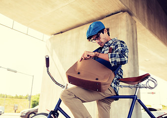 Image showing hipster man with bicycle looking something in bag