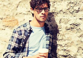 Image showing man in eyeglasses drinking coffee over street wall