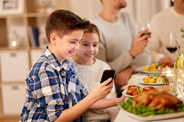 Image showing boy with sister using smartphone at family dinner