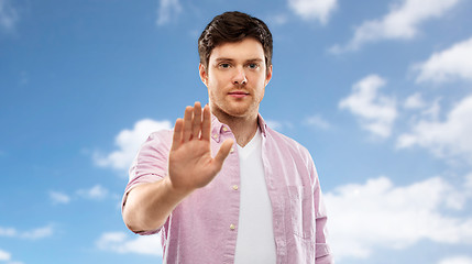 Image showing young man showing stop gesture over blue sky