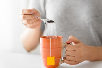 Image showing close up of woman adding sugar to cup of tea