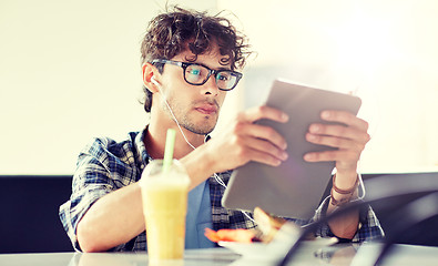 Image showing man with tablet pc and earphones sitting at cafe