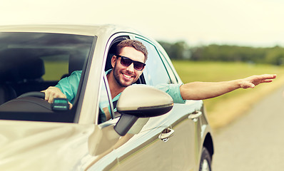 Image showing happy man in shades driving car and waving hand