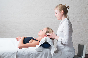 Image showing Professional female masseur giving relaxing massage treatment to young female client. Hands of masseuse on forehead of young lady during procedure of spa facial massage