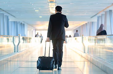 Image showing Businessman walking and wheeling a trolley suitcase at the lobby, talking on a mobile phone. Business travel concept.