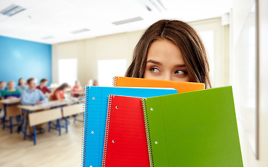 Image showing student girl hiding behind notebooks at school