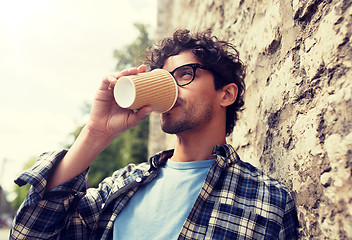 Image showing man in eyeglasses drinking coffee over street wall