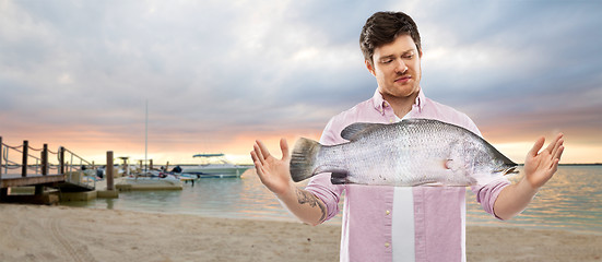 Image showing displeased young man showing size of fish on beach