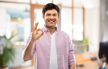 Image showing smiling young man showing ok hand sign over office