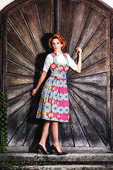 Image showing Portrait of a beautiful young woman in a dirndl, standing on a wooden wall.