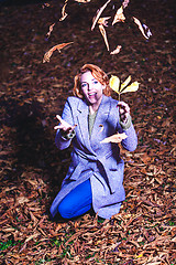 Image showing Portrait of a young woman kneeling on the leaves in autumn and throwing this up.