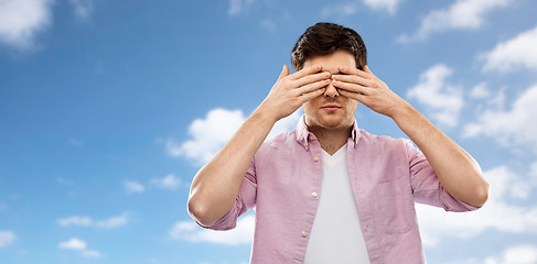 Image showing man closing his eyes by hands over blue sky