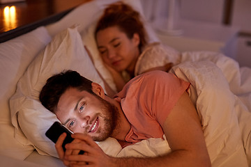 Image showing man using smartphone while girlfriend is sleeping