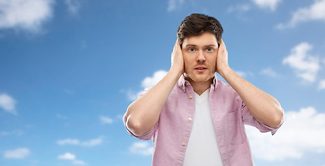 Image showing man closing ears by hands over blue sky