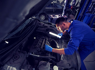 Image showing mechanic man with lamp repairing car at workshop