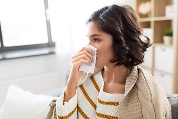 Image showing sick woman blowing nose in paper tissue at home